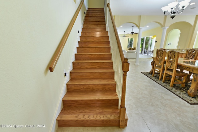 stairs featuring ceiling fan with notable chandelier, ornate columns, and tile patterned floors