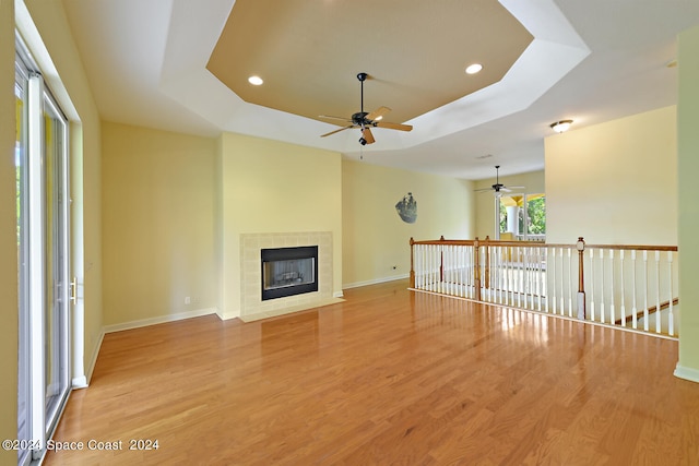 unfurnished living room featuring light wood-type flooring, a raised ceiling, a fireplace, and ceiling fan