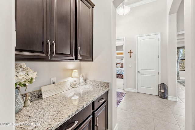 kitchen with ornamental molding, light stone countertops, and dark brown cabinets