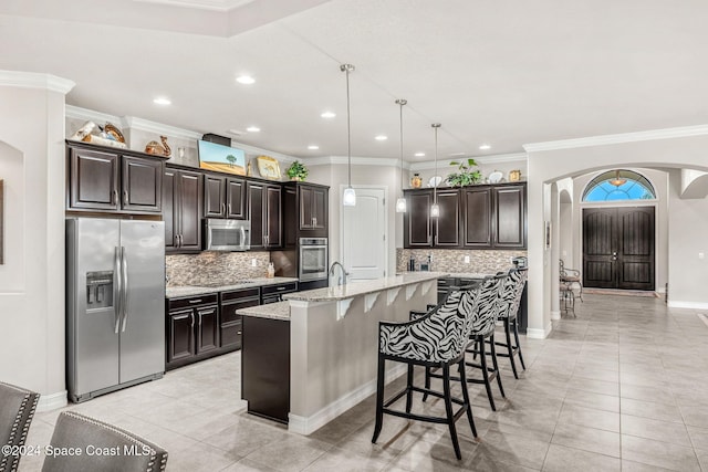 kitchen with light stone countertops, appliances with stainless steel finishes, dark brown cabinetry, pendant lighting, and a center island with sink