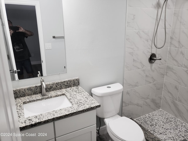 bathroom featuring a tile shower, vanity, and toilet