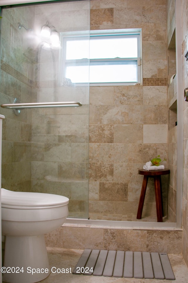 bathroom with a wealth of natural light, a shower with door, and toilet