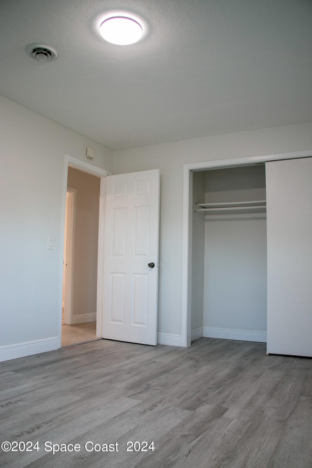 unfurnished bedroom with a textured ceiling, light hardwood / wood-style floors, and a closet