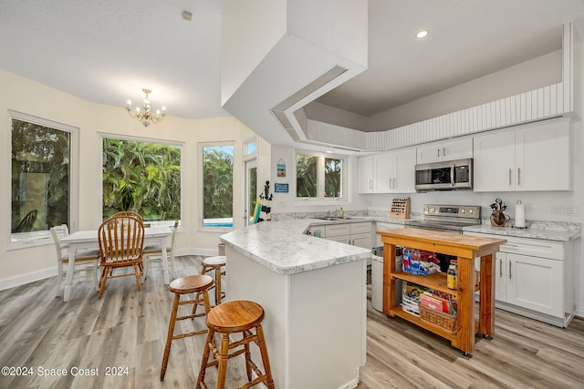 kitchen with light hardwood / wood-style floors, a notable chandelier, appliances with stainless steel finishes, a kitchen bar, and white cabinetry