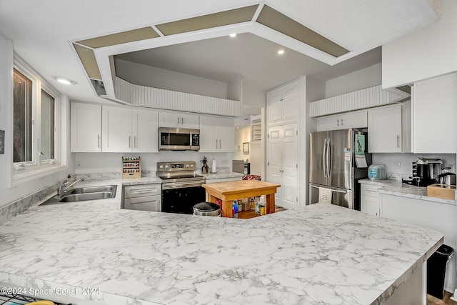 kitchen with stainless steel appliances, kitchen peninsula, sink, and white cabinetry