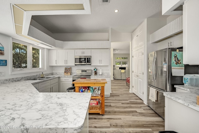 kitchen with stainless steel appliances, light hardwood / wood-style floors, white cabinets, and a healthy amount of sunlight