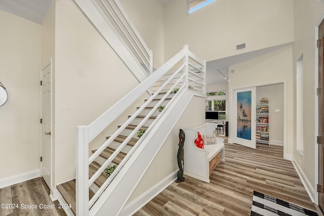 stairway with wood-type flooring and a high ceiling