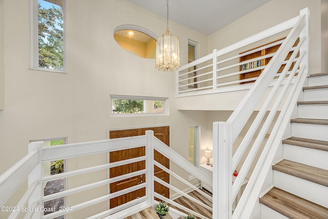 stairway with hardwood / wood-style flooring, plenty of natural light, and a chandelier