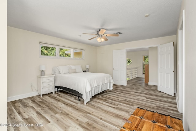 bedroom with ceiling fan, a textured ceiling, and light hardwood / wood-style flooring