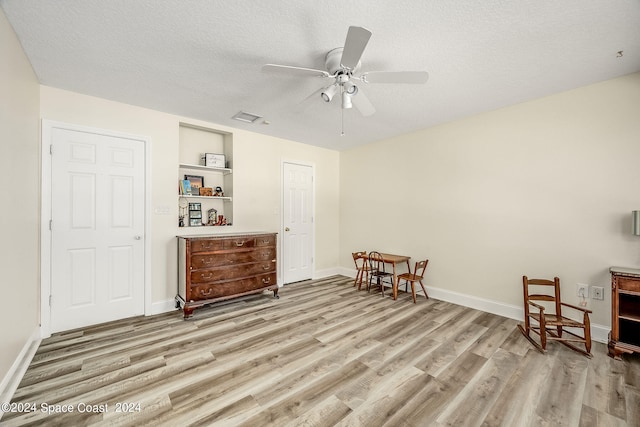 living area with built in shelves, light hardwood / wood-style flooring, a textured ceiling, and ceiling fan