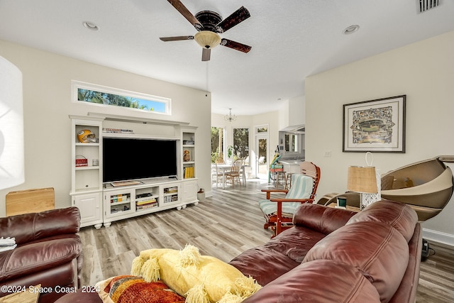 living room featuring ceiling fan with notable chandelier, a textured ceiling, and light hardwood / wood-style flooring