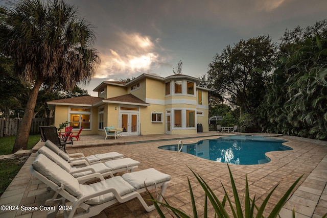 pool at dusk with french doors and a patio area