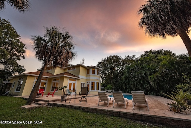 back house at dusk with a patio and a yard