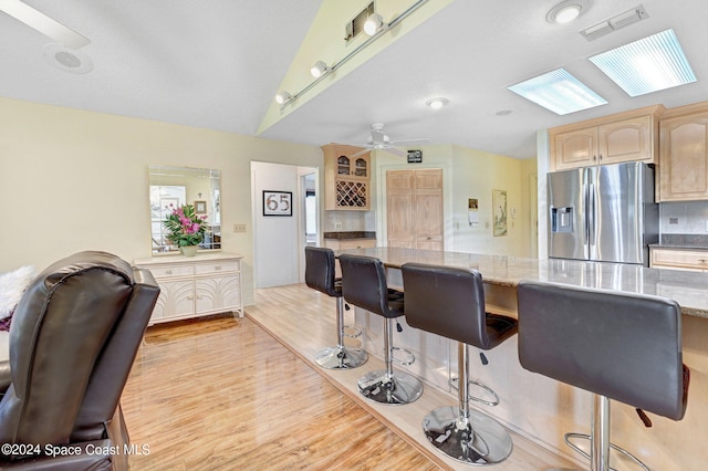 kitchen featuring decorative backsplash, stainless steel fridge, light brown cabinetry, ceiling fan, and light hardwood / wood-style flooring