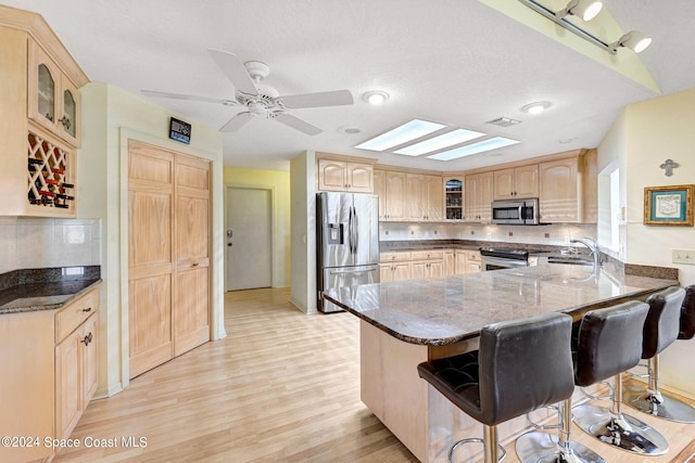 kitchen with a kitchen bar, sink, appliances with stainless steel finishes, light hardwood / wood-style floors, and kitchen peninsula