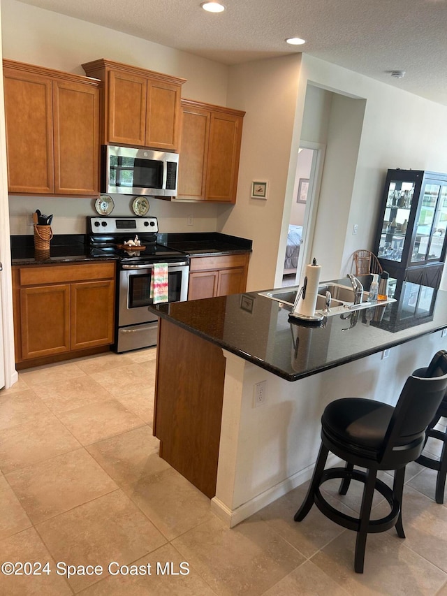 kitchen with a breakfast bar, a textured ceiling, appliances with stainless steel finishes, and light tile patterned flooring