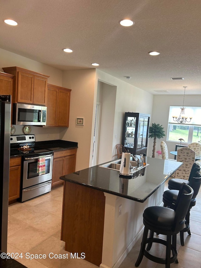 kitchen featuring a notable chandelier, stainless steel appliances, sink, and an island with sink