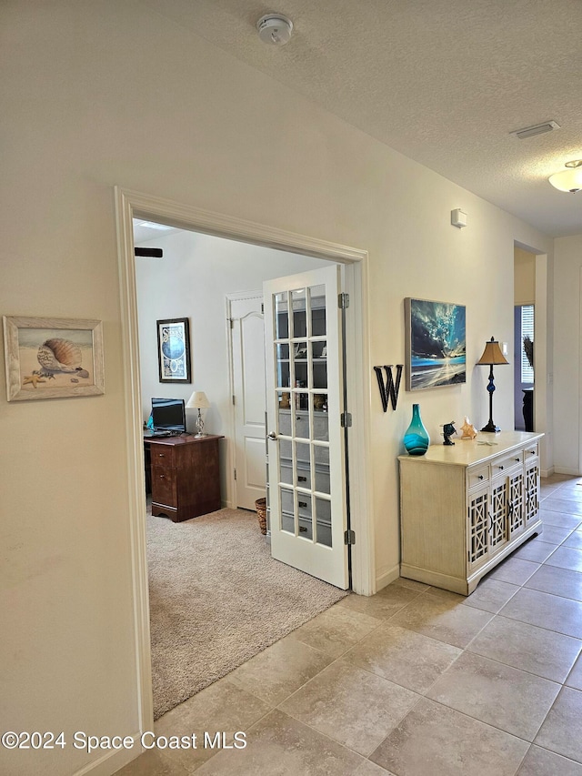 corridor with light colored carpet and a textured ceiling