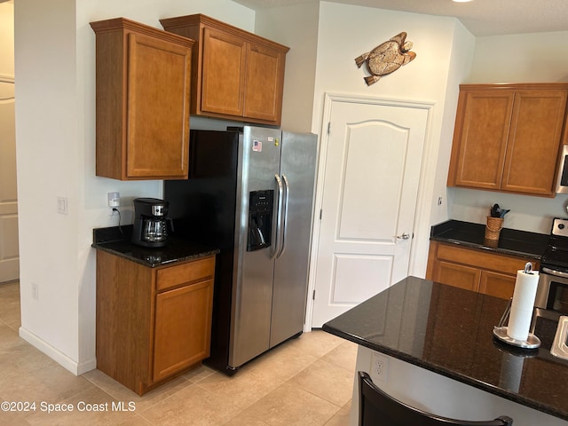 kitchen featuring light tile patterned floors, stainless steel appliances, and dark stone countertops