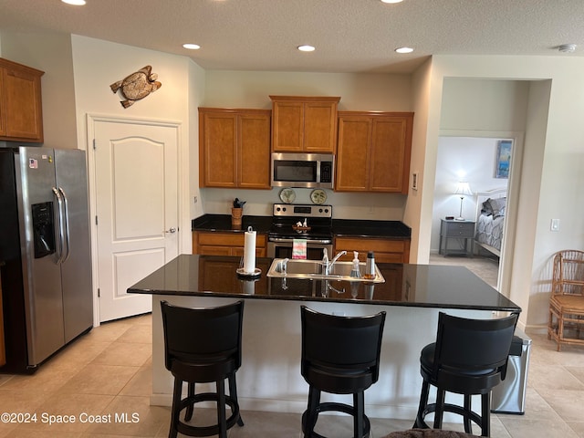 kitchen featuring sink, light tile patterned floors, stainless steel appliances, and an island with sink