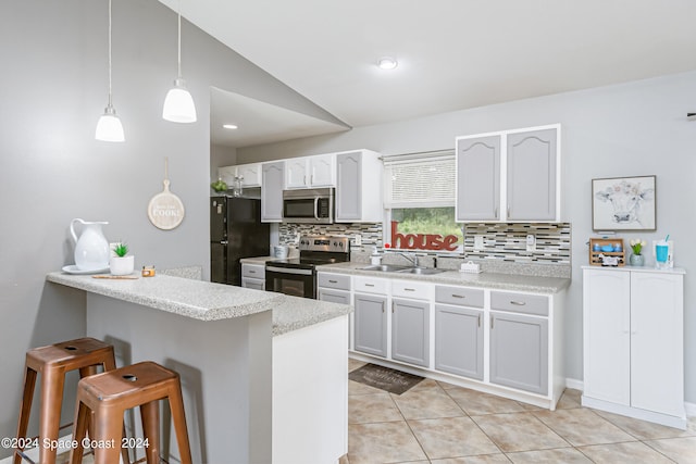 kitchen with lofted ceiling, hanging light fixtures, white cabinetry, stainless steel appliances, and a kitchen bar