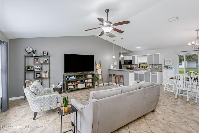 tiled living room with ceiling fan with notable chandelier and vaulted ceiling