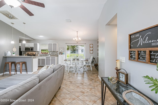 living room with lofted ceiling, ceiling fan with notable chandelier, and light tile patterned floors