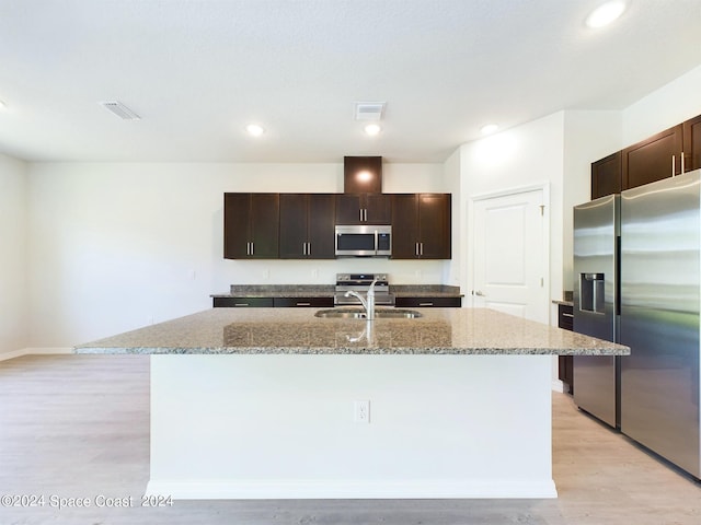 kitchen featuring appliances with stainless steel finishes, dark brown cabinetry, a kitchen island with sink, and light hardwood / wood-style flooring