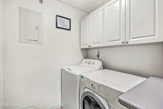 laundry room featuring a textured ceiling, electric panel, washer and dryer, and cabinets