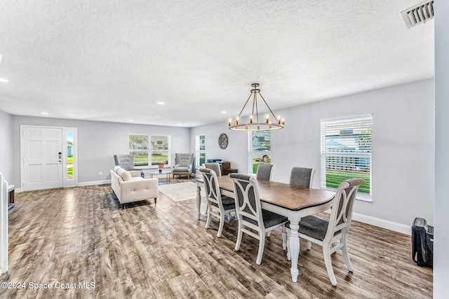 dining space featuring a textured ceiling, wood-type flooring, an inviting chandelier, and plenty of natural light