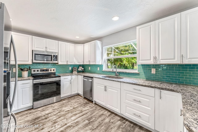 kitchen with stainless steel appliances, sink, white cabinets, a textured ceiling, and light hardwood / wood-style floors