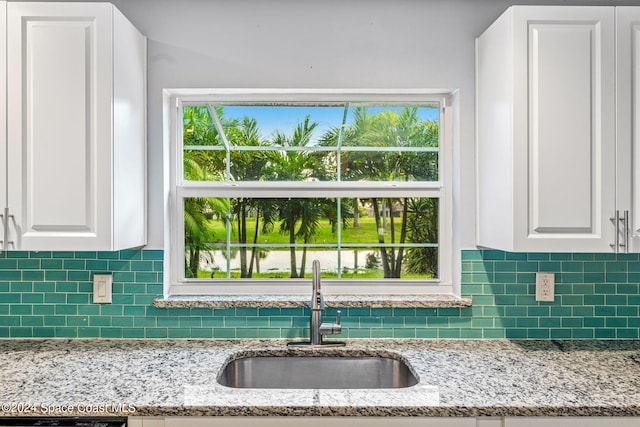 kitchen featuring light stone counters, a sink, white cabinets, and tasteful backsplash