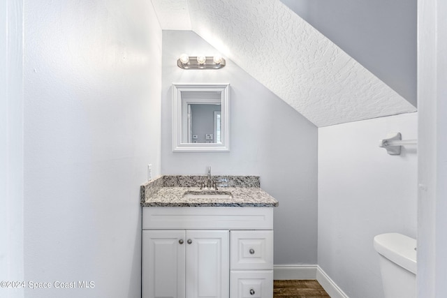 half bathroom featuring vanity, a textured ceiling, baseboards, wood finished floors, and lofted ceiling