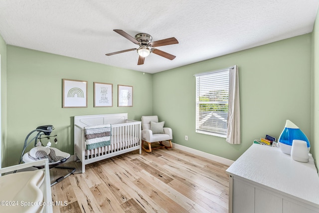 bedroom featuring a textured ceiling, a crib, light wood-type flooring, and ceiling fan