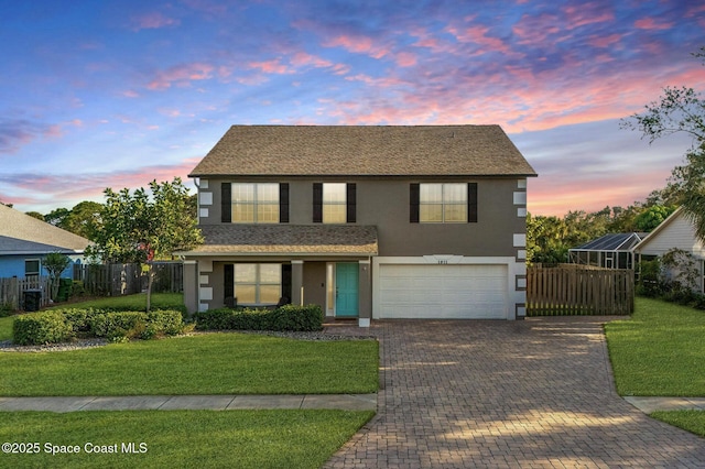 traditional home featuring a garage, fence, a front yard, decorative driveway, and stucco siding
