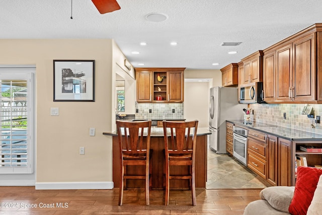 kitchen featuring stainless steel appliances, light hardwood / wood-style floors, decorative backsplash, and a textured ceiling