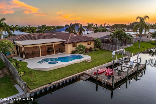 pool at dusk with an in ground hot tub, a patio, a dock, a lawn, and a water view