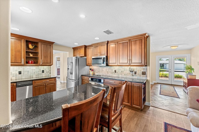 kitchen featuring french doors, appliances with stainless steel finishes, dark stone counters, a kitchen bar, and dark hardwood / wood-style flooring