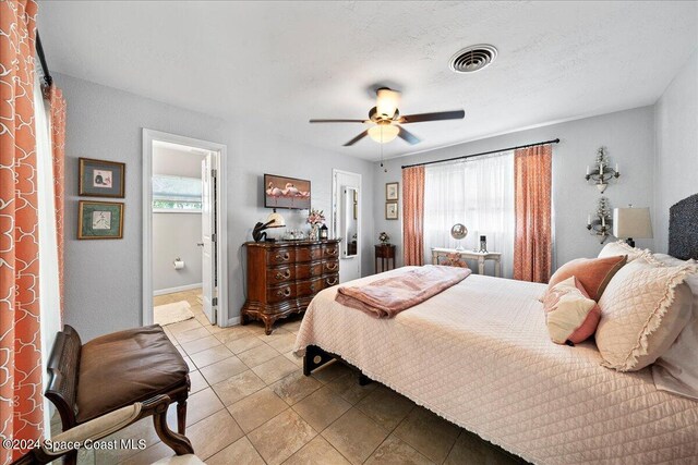 tiled bedroom featuring multiple windows, ceiling fan, and connected bathroom