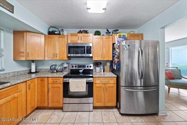 kitchen featuring appliances with stainless steel finishes, light stone counters, light tile patterned floors, and a textured ceiling