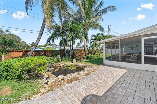 view of patio featuring fence, a sunroom, and a small pond