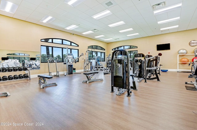 exercise room featuring a paneled ceiling, baseboards, visible vents, and wood finished floors