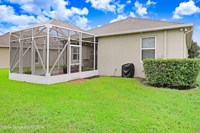 rear view of property featuring a shingled roof, a lanai, a yard, and stucco siding