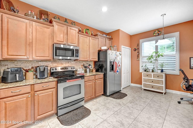 kitchen with light stone counters, stainless steel appliances, pendant lighting, light tile patterned floors, and backsplash