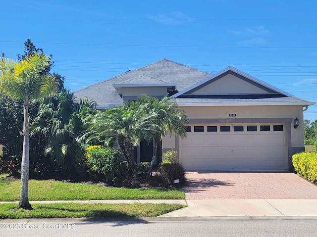 view of front of property with an attached garage, roof with shingles, decorative driveway, and stucco siding