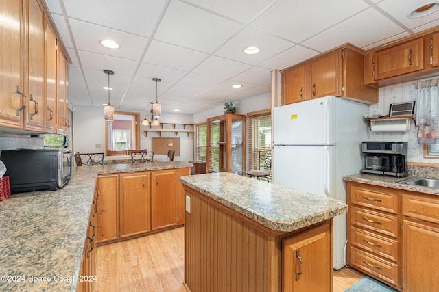 kitchen with white refrigerator, light hardwood / wood-style floors, tasteful backsplash, a kitchen island, and decorative light fixtures