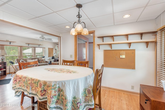 dining area with ceiling fan with notable chandelier, light wood-type flooring, and a paneled ceiling