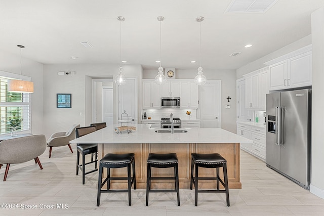 kitchen with appliances with stainless steel finishes, sink, pendant lighting, white cabinets, and a center island with sink