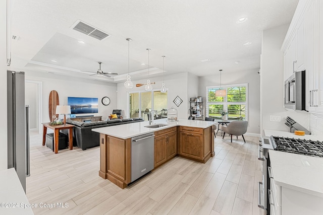 kitchen with appliances with stainless steel finishes, an island with sink, a raised ceiling, hanging light fixtures, and white cabinetry