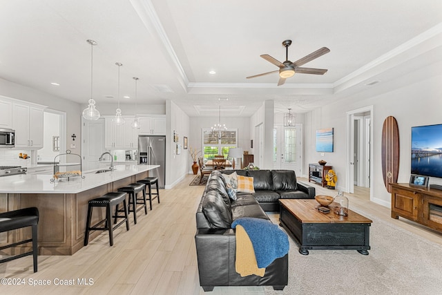 living room featuring a raised ceiling, ornamental molding, ceiling fan with notable chandelier, light hardwood / wood-style floors, and sink